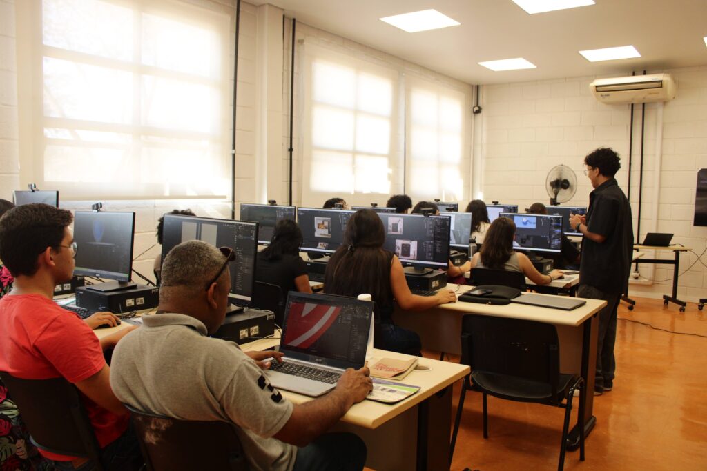 Participantes acompanham oficina de modelagem 3D em laboratório de informática, utilizando computadores enquanto o facilitador orienta a atividade.